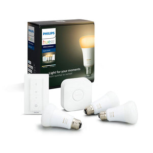 A Philips hue white ambient smart lighting starter kit 3 bulbs, a hub and a dimmer switch sit in front of its packaging