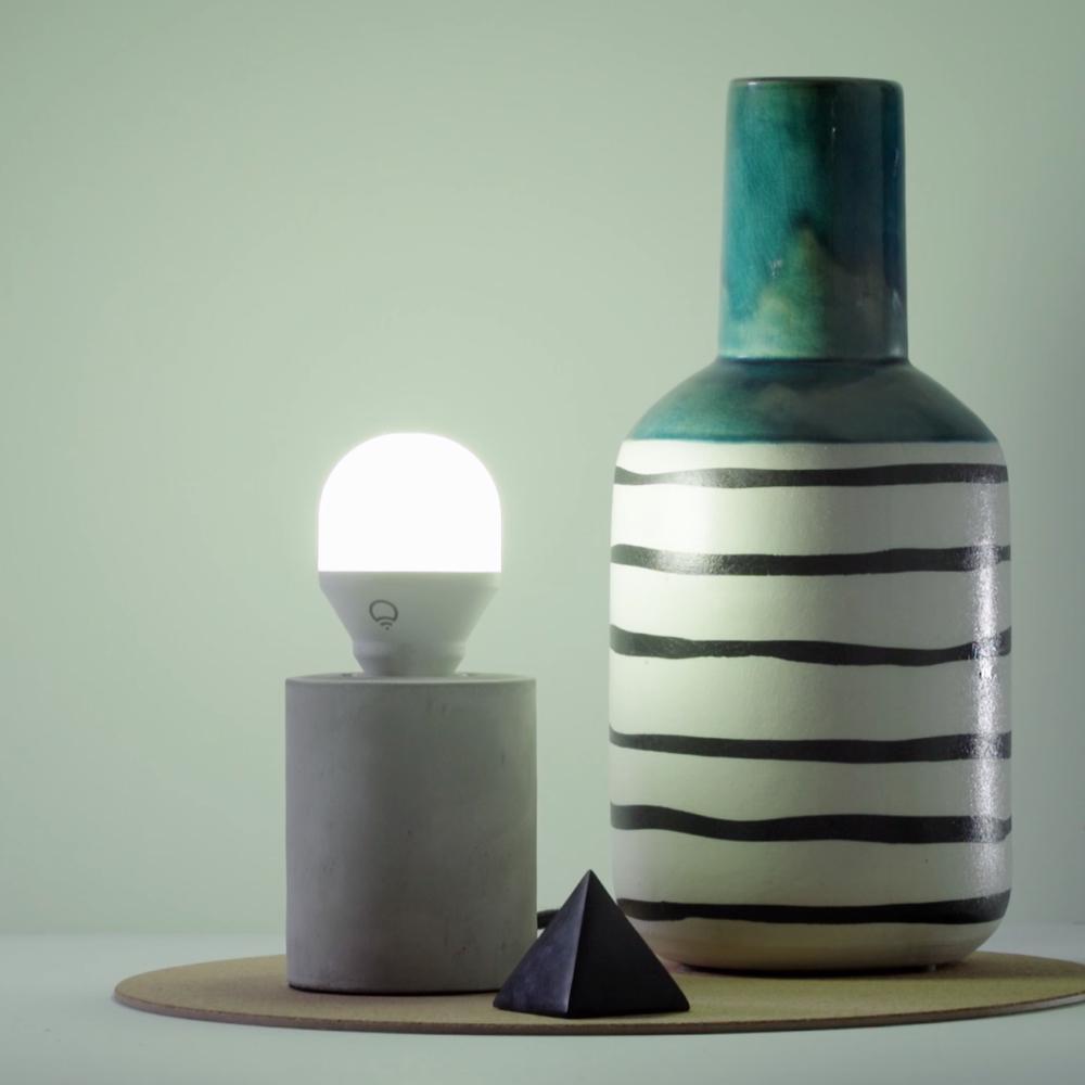 White light in a lamp next to a vase and pyramid ornament
