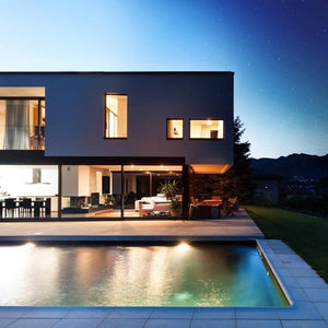 outside of a modern house with well lit windows and a lit pool in front