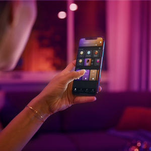 a hand holding a mobile phone using the philips hue app.  purple background lighting.