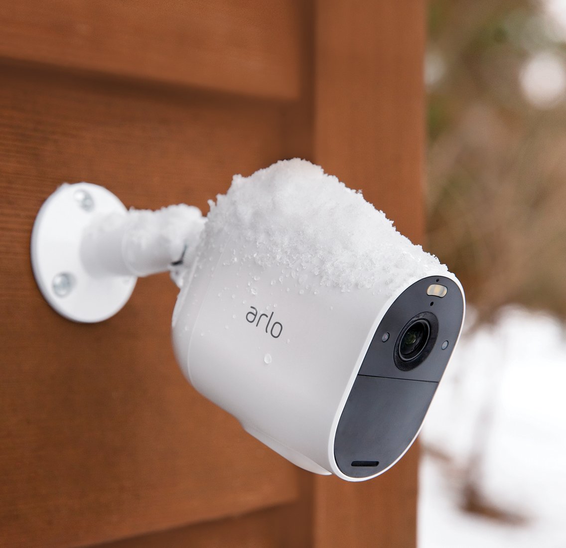 An Arlo essential spotlight covered in snow and mounted to a wooden shed.