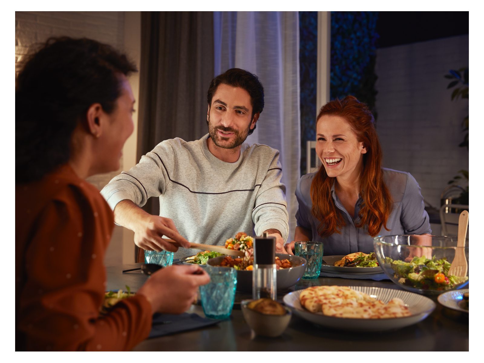 3 people sitting around a table with plates of food and glasses 