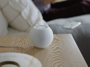 An apple homepod mini white smart speaker sitting on a wooden table