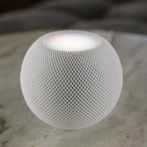 A white apple homepod mini, smart home speaker with its top light shining white