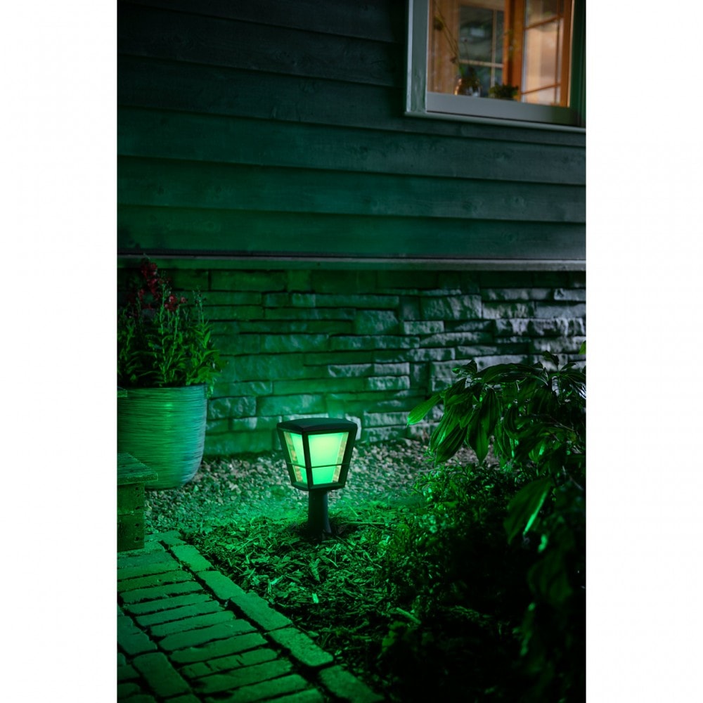 A philips hue Econic style, outdoor pedestal shining a green light near a brick path