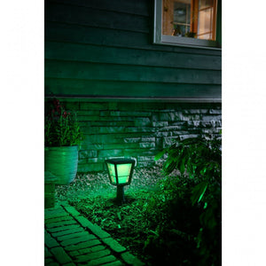 A philips hue Econic style, outdoor pedestal shining a green light near a brick path