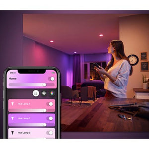 A person holding a phone in a room with 3 spotlights and the mobile phone screen view showing the philips hue app being used