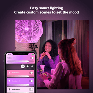2 people sitting at a table with a violet coloured light shining over them and a mobile phone showing the philips hue app in the bottom left