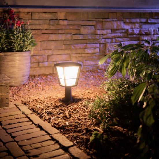 A philips hue Econic style, outdoor pedestal shining a white light near a brick path