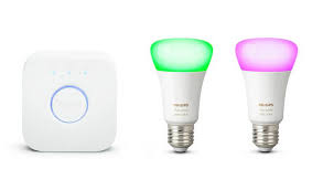 The philips hue hub next to two E27 philips hue colour smart light bulbs showing pink and green light effects