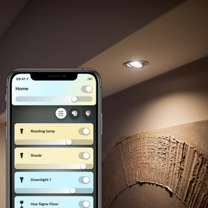 A bright white spotlight shining on to a piece of wall art.  A mobile phone showing the philips hue app controlling the light in the bottom left