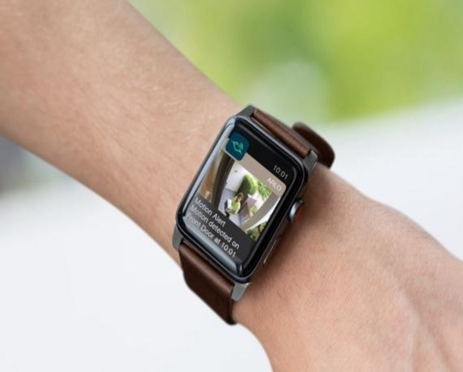 an apple smart watch on someones wrist showing the arlo app integration - image on the watch shows a person at a front door with a parcel 